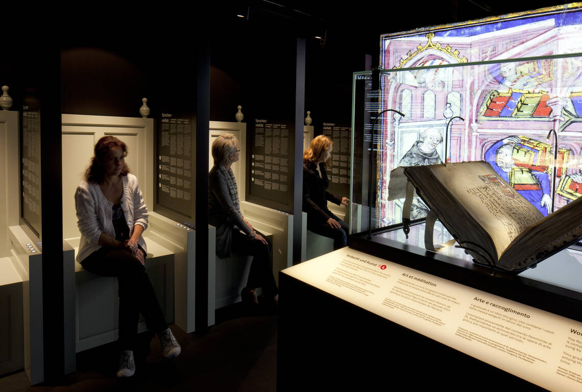 Three ladies sitting in the staged scritorium listening to a scholar