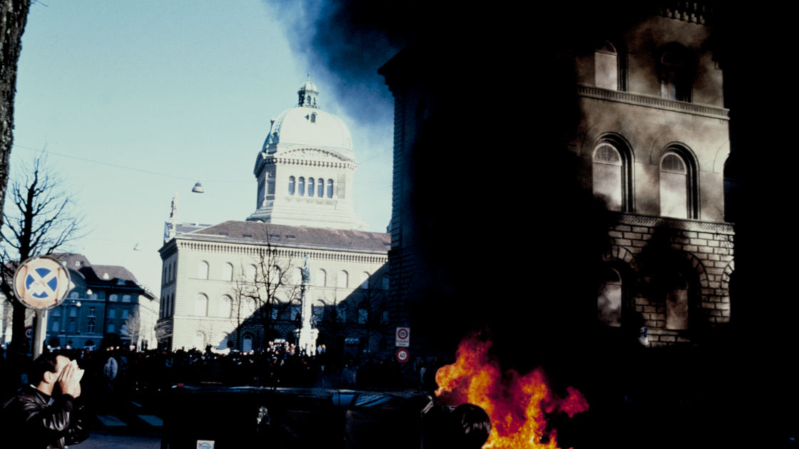 Fire and smoke during the demonstration of the Secret files scandal, with the Federal Palace in the background